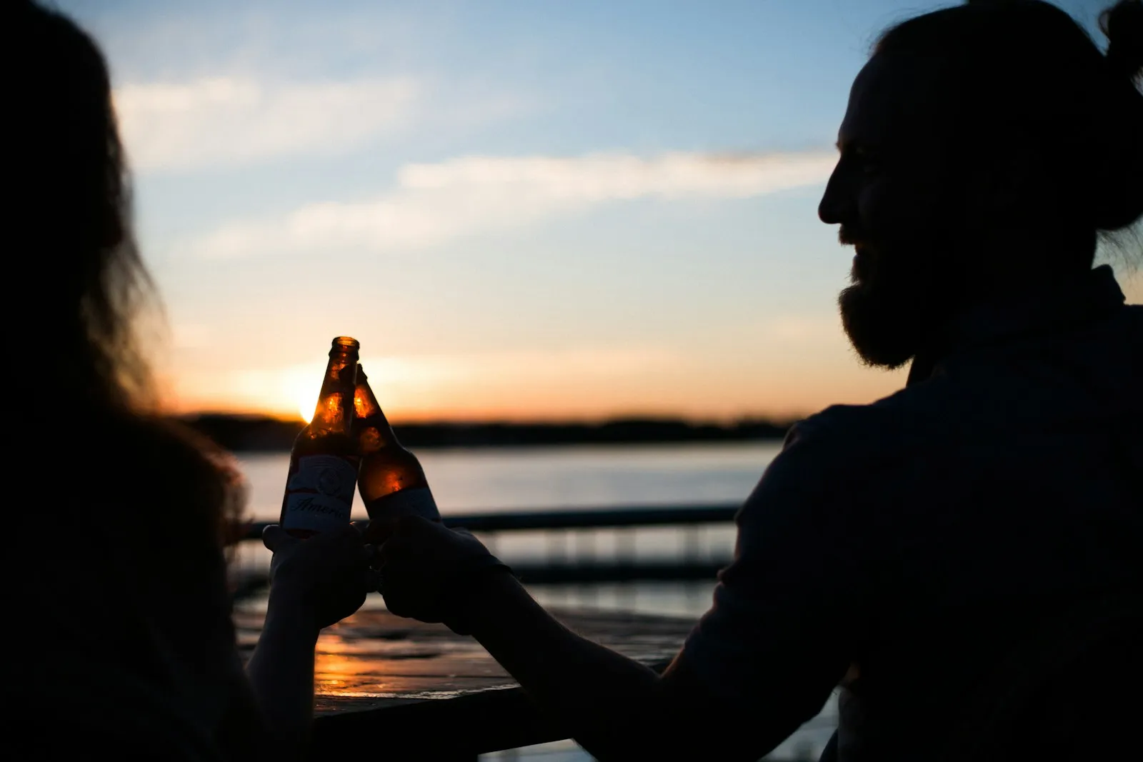 Coppia brinda con una birra a bordo di una barca al tramonto
