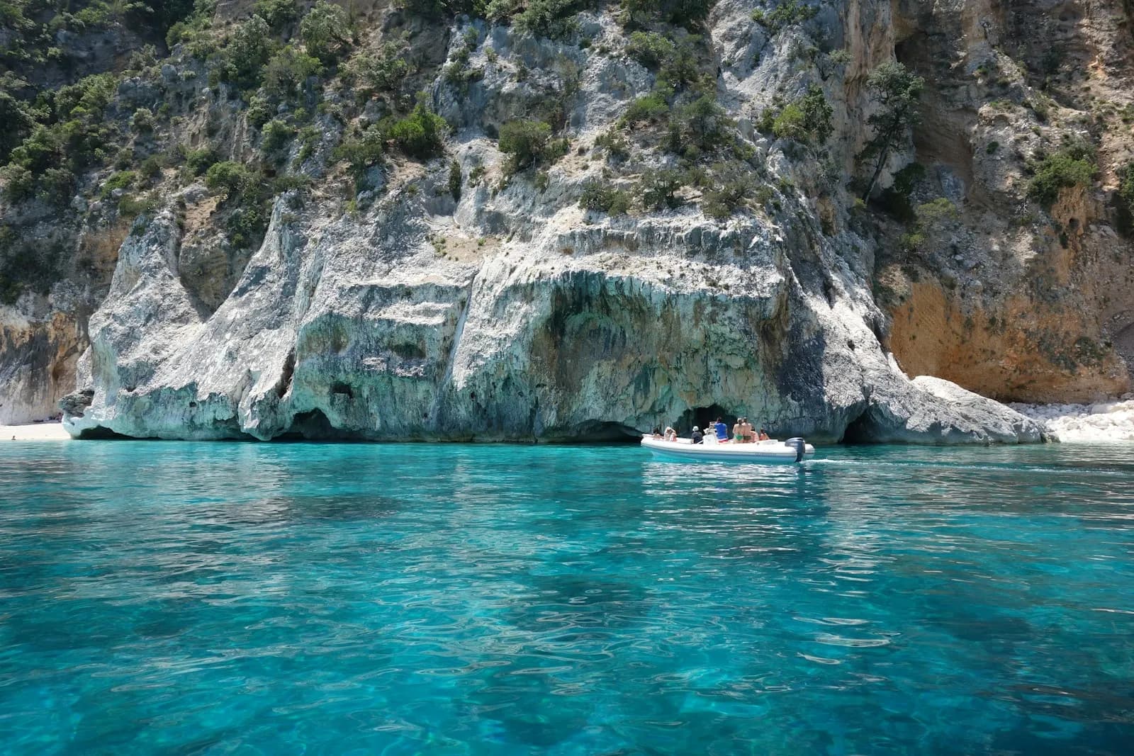 Una barca sotto le alte falesie bianche di una cala del Golfo di Orosei, a Cala Gonone