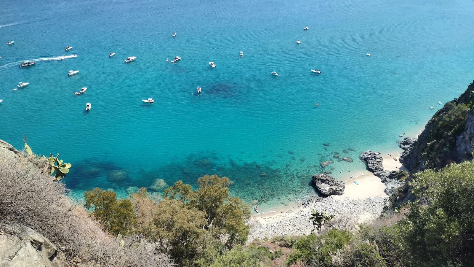 Piccole imbarcazioni ancorate in una cala turchese della costa calabrese