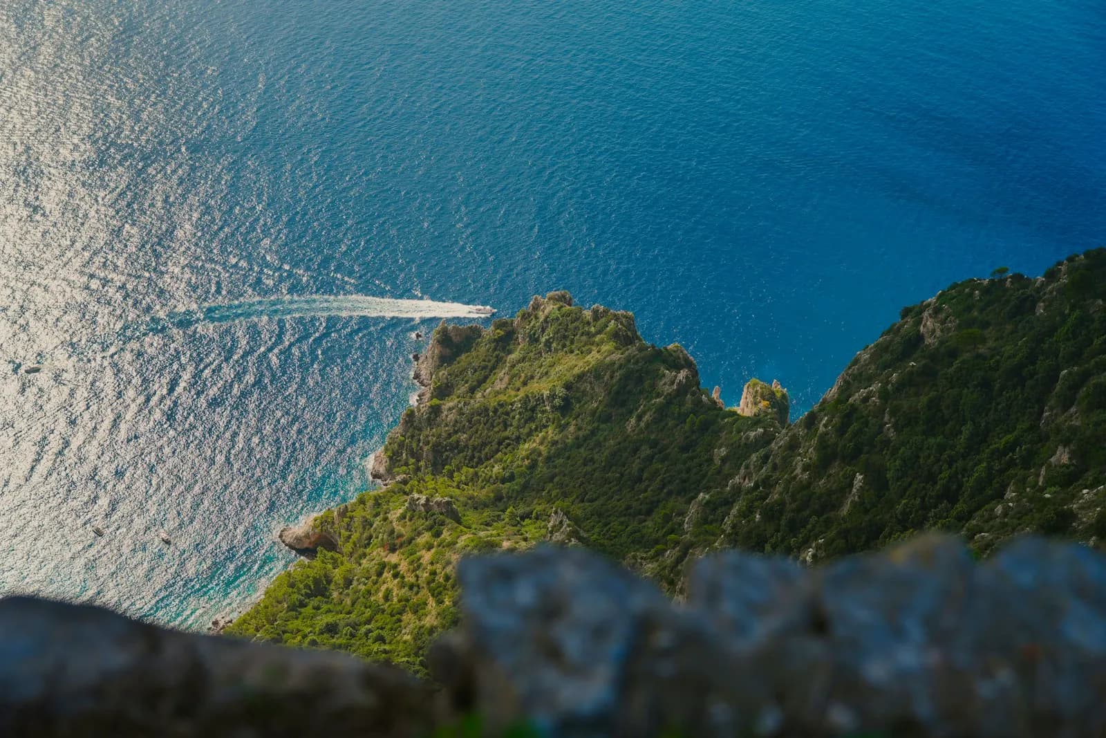 Una barca naviga sotto le coste verdi di Capri nel mare azzurro