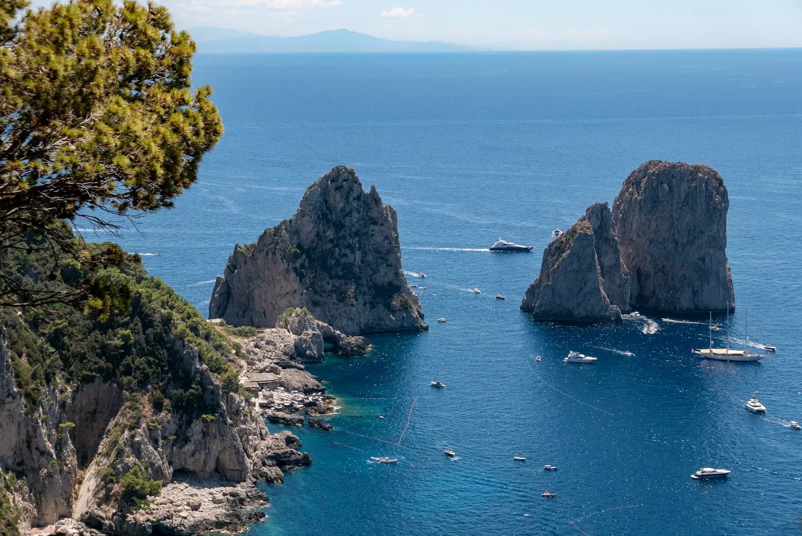 I Faraglioni di Capri visti dalla costa con alcune barche nel mare blu