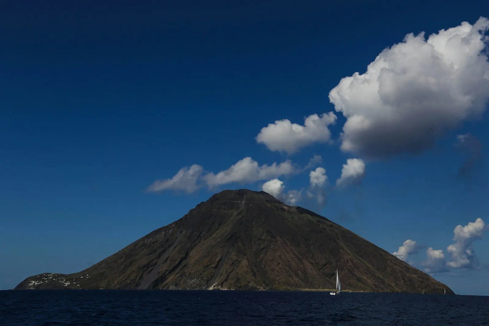 Barca a vela davanti a un'isola vulcanica delle Isole Eolie