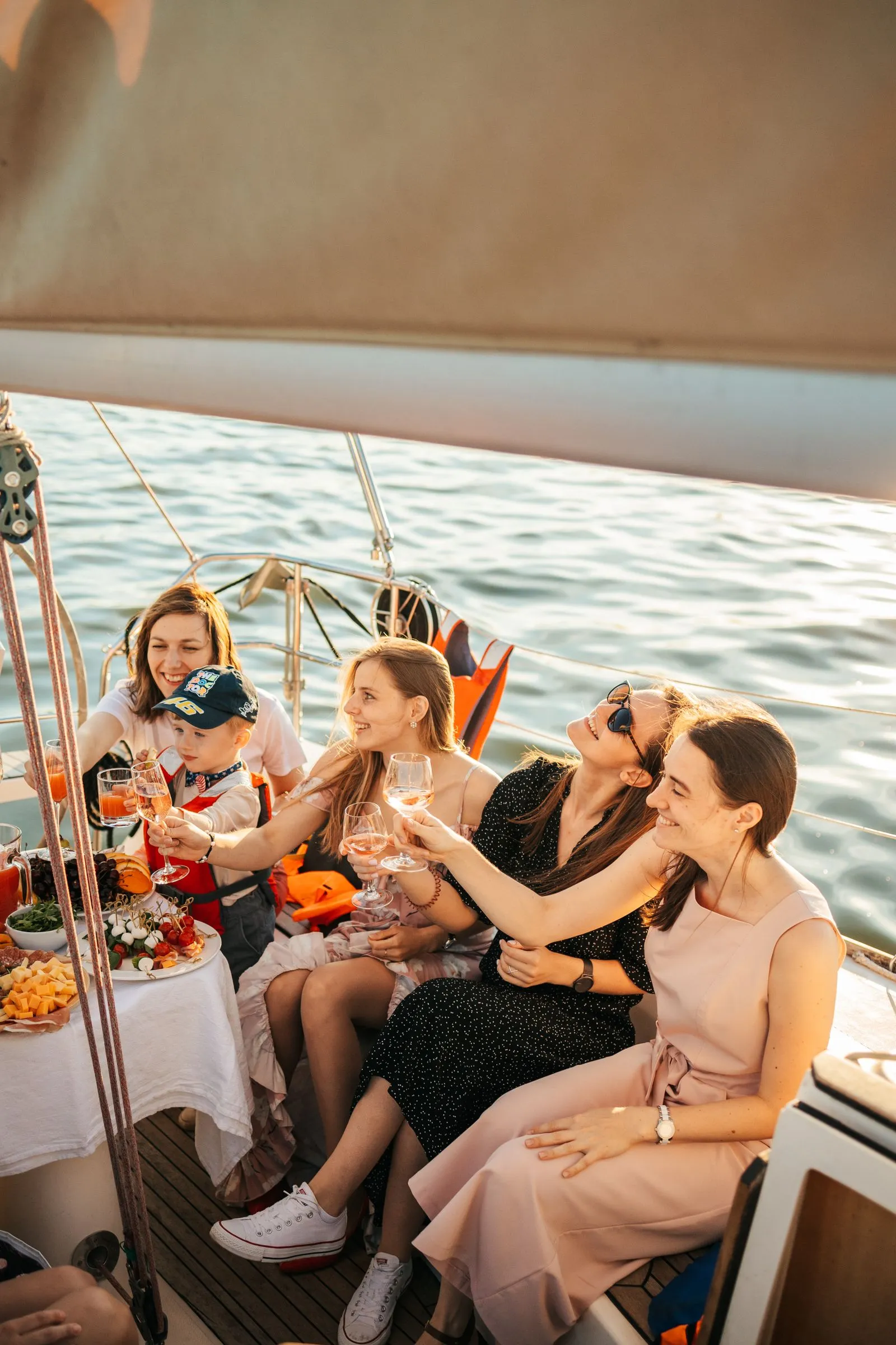 Gruppo di amici brinda a bordo di una barca a vela con tavola imbandita al tramonto