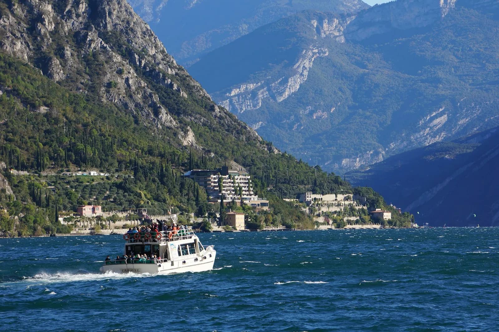 Barca di linea con passeggeri a bordo naviga sul Lago di Garda vicino a Limone, montagne sullo sfondo
