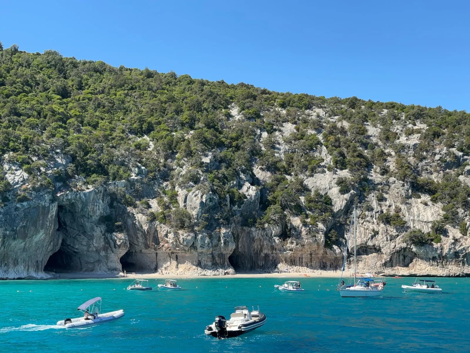 Gommoni e piccole barche all'ancora in una baia dall'acqua turchese lungo una costa rocciosa