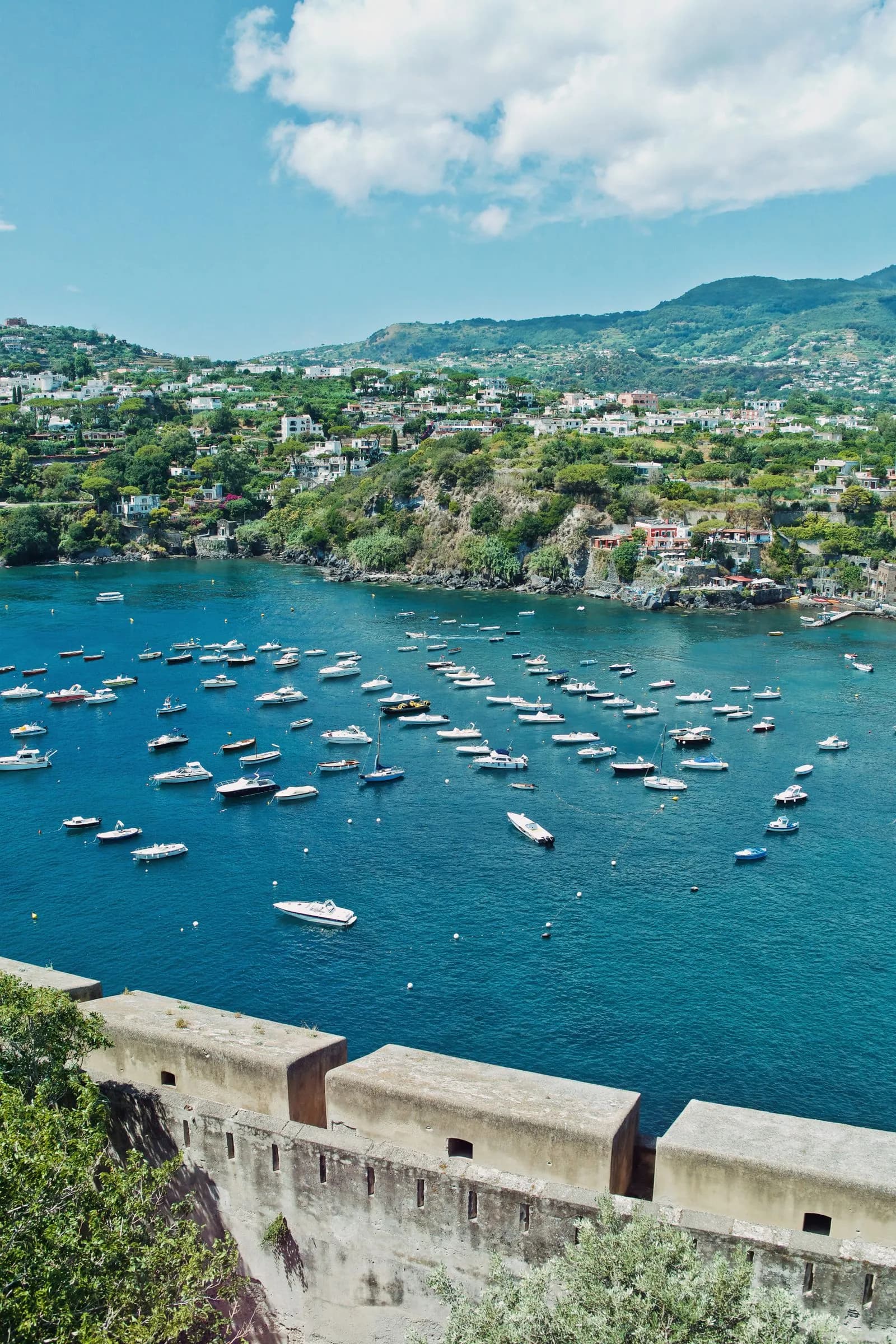 Decine di piccole barche ormeggiate in una baia turchese di Ischia vista dall'alto