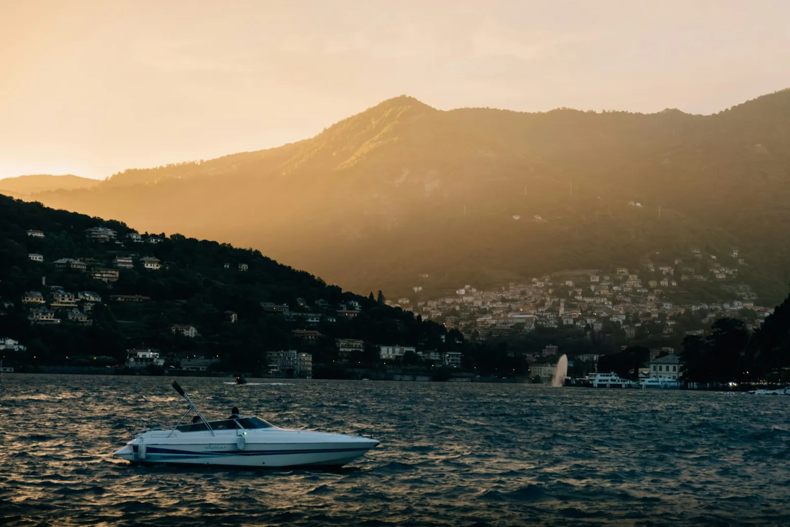 Piccola barca a motore al tramonto sul Lago di Como con un borgo lacustre sullo sfondo