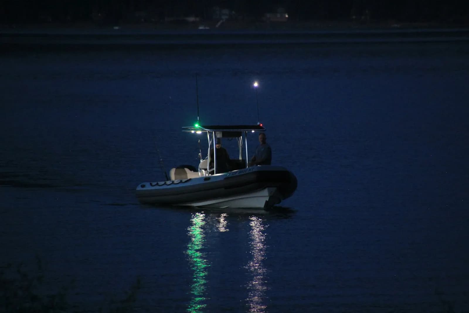 Piccolo gommone in navigazione notturna con luce laterale verde visibile e riflesso sull'acqua scura