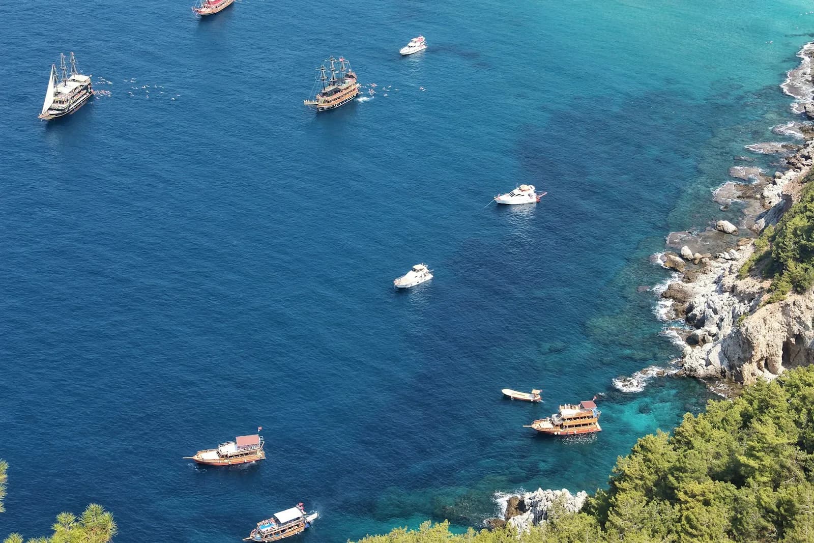 Barche a motore e a vela all'ancora nelle acque blu di una baia lungo una costa rocciosa