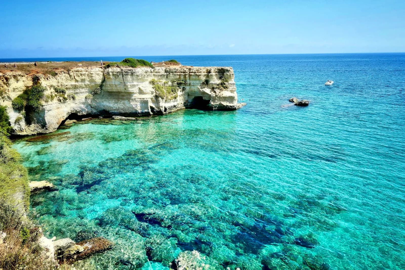 Una piccola barca tra gli scogli e l'acqua turchese della costa di Otranto, ai Faraglioni di Torre Sant'Andrea