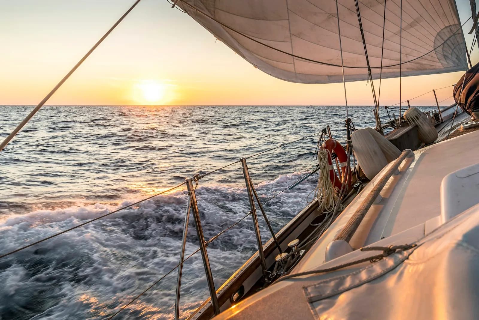 Barca a vela in navigazione al tramonto, vista dal ponte verso le vele