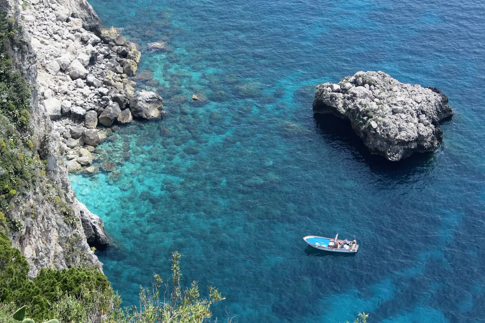 Caletta italiana con acqua turchese, scogliere e piccole barche all'ancora