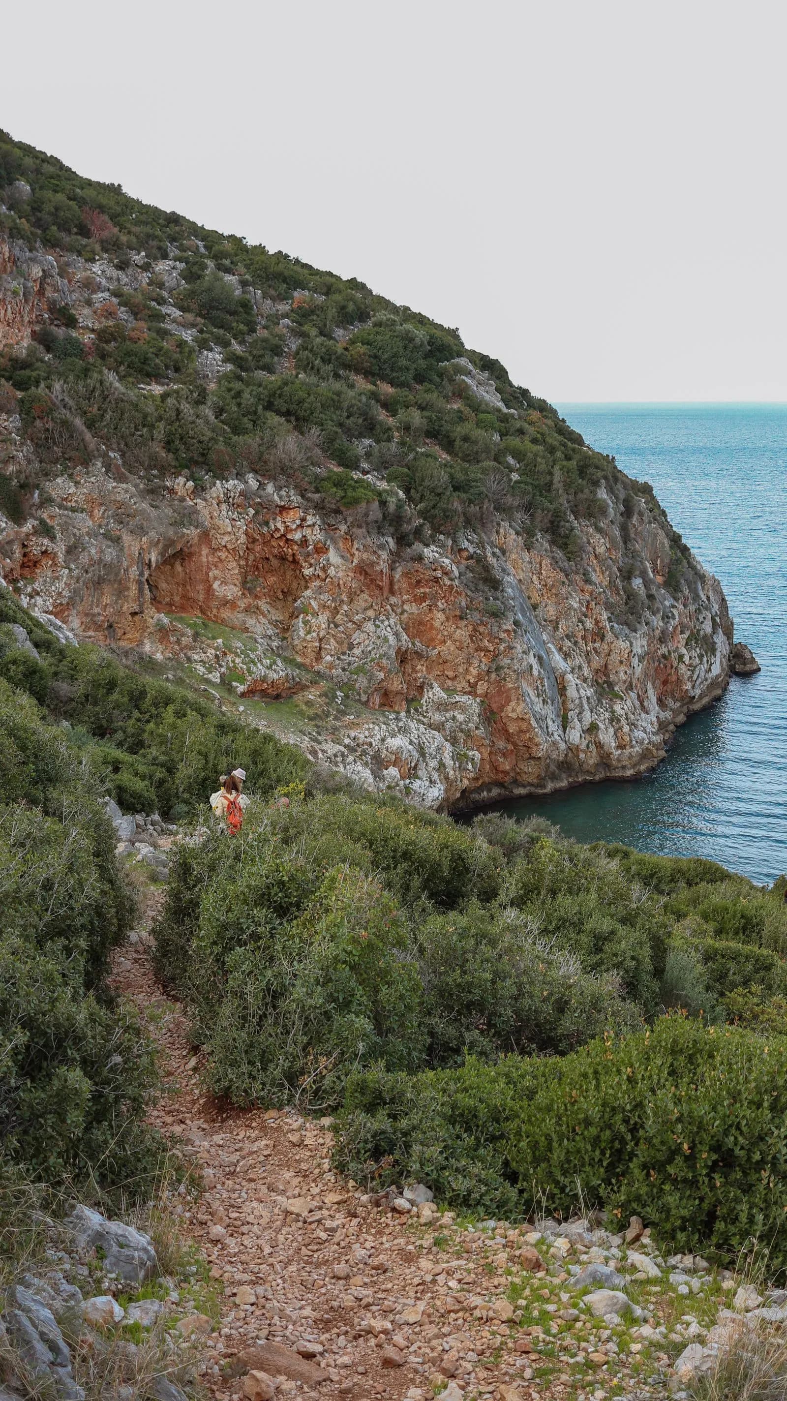 Sentiero escursionistico tra la macchia mediterranea con scogliera rocciosa e mare cristallino