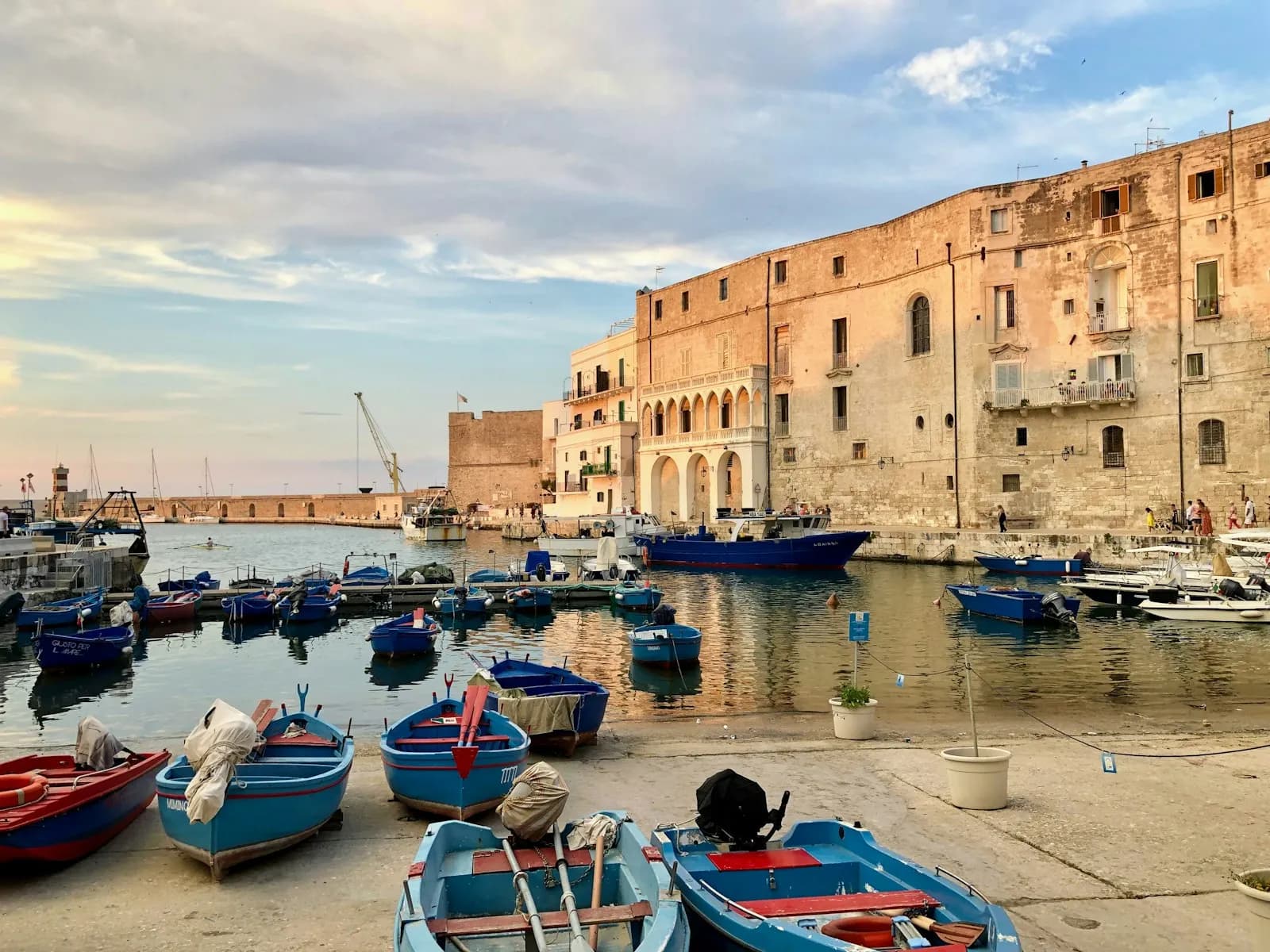 Porticciolo pugliese con edifici in pietra chiara e piccole barche da pesca colorate