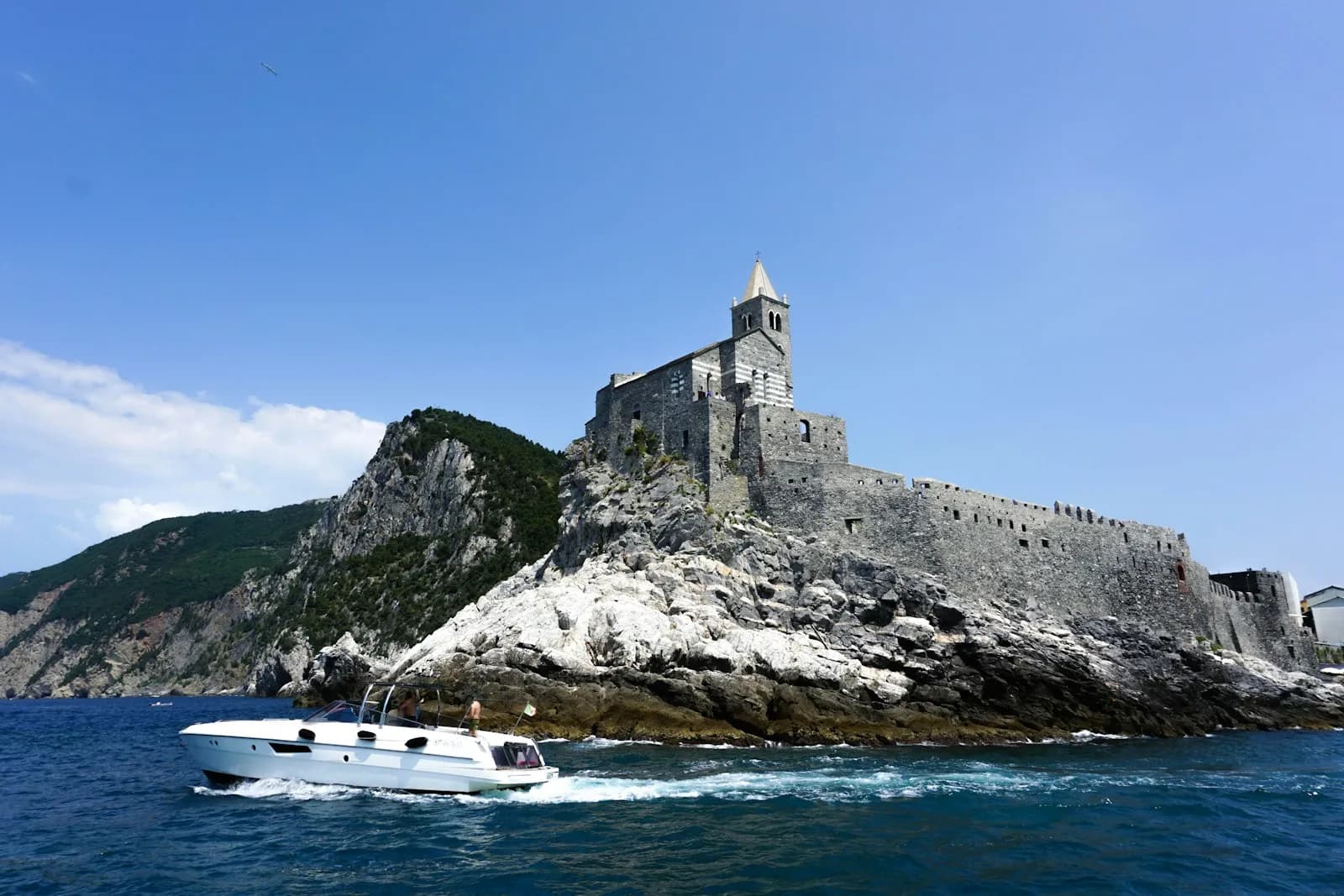 La chiesa di San Pietro a Portovenere sul promontorio roccioso, con una barca a motore che passa in primo piano