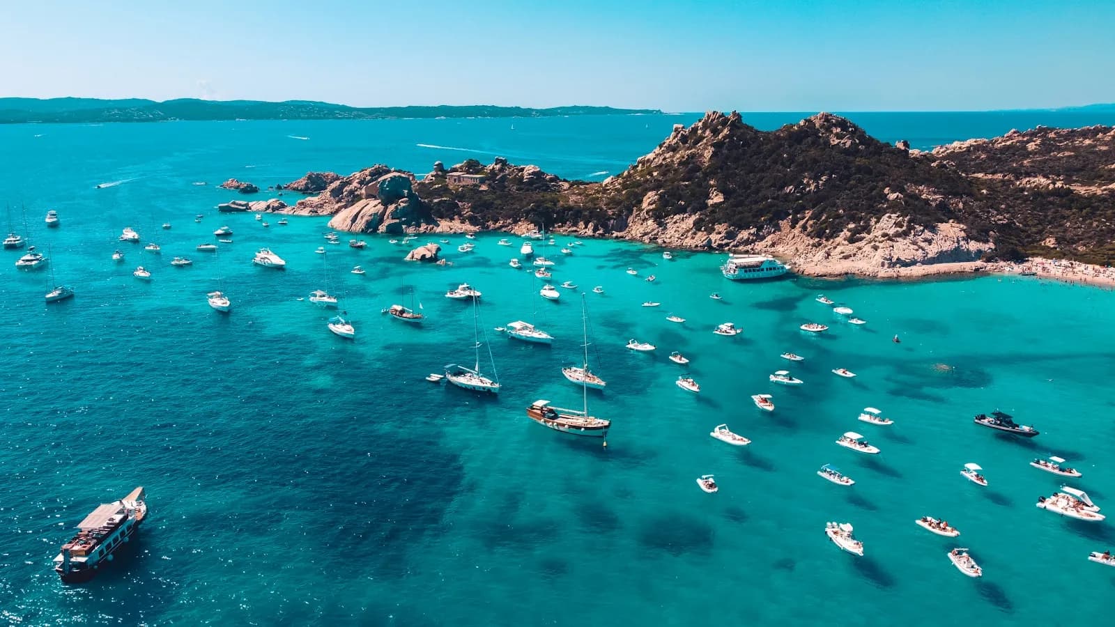Numerose barche a vela e a motore all'ancora nelle acque turchesi di una cala della Sardegna