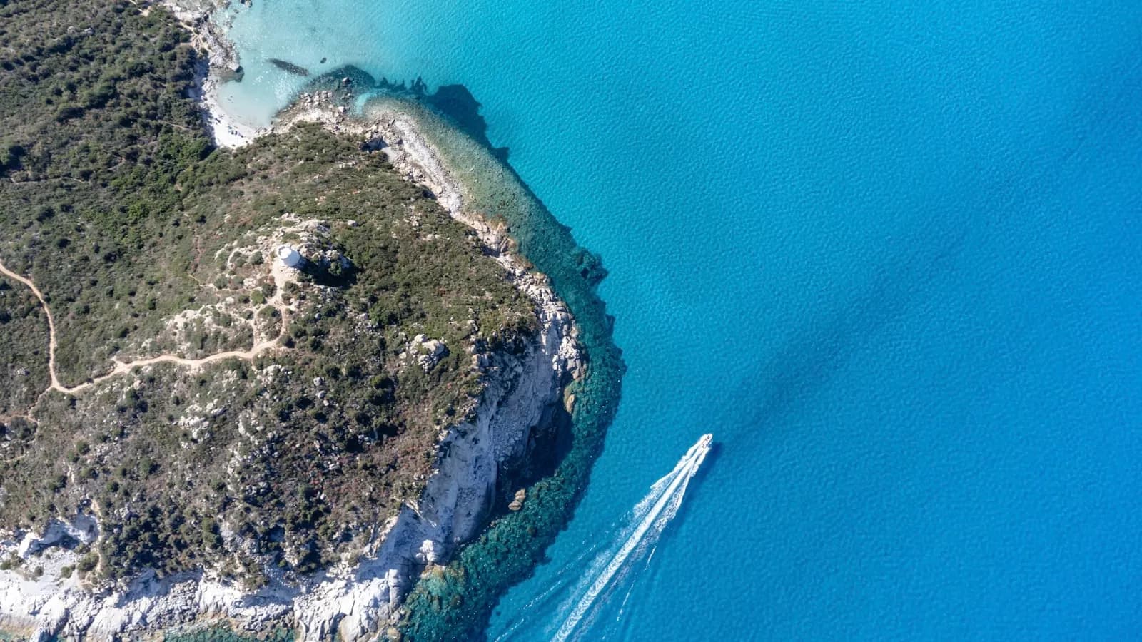 Una barca su acque turchesi lungo una costa rocciosa della Sardegna