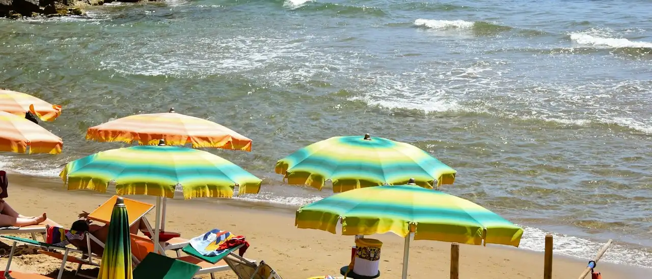 Ombrelloni colorati di un lido sulla spiaggia di Sperlonga con la Torre Truglia sul promontorio