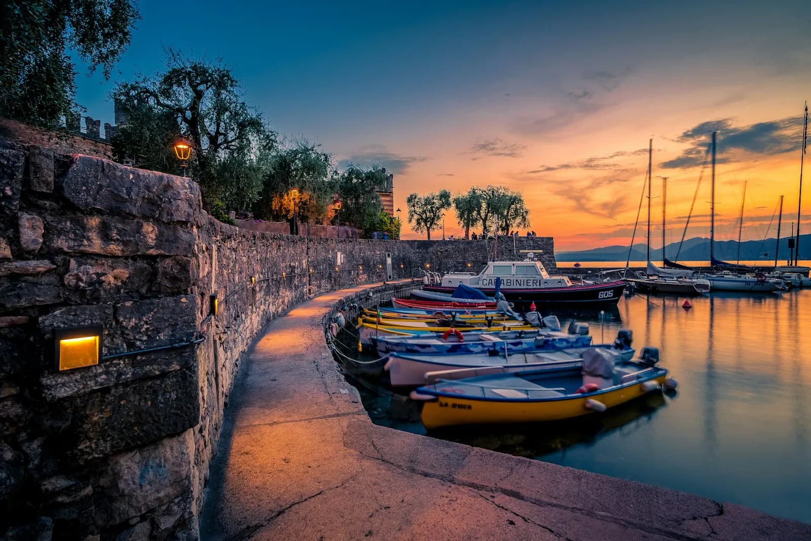 Barche colorate ormeggiate lungo il porto di Torri del Benaco al tramonto sul Lago di Garda