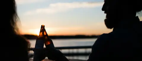 Coppia brinda con una birra a bordo di una barca al tramonto
