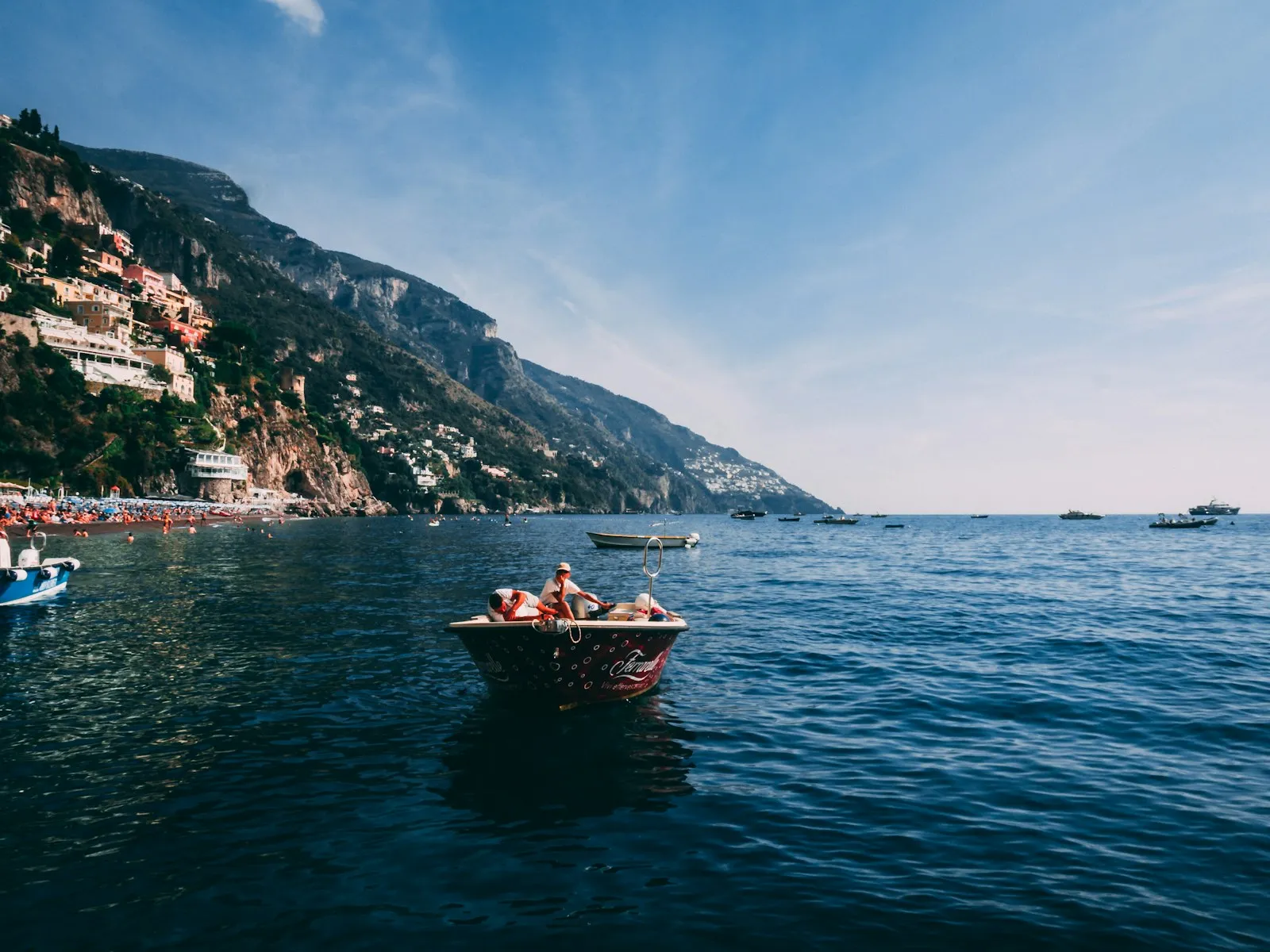Piccola barca aperta con persone a bordo sotto una costa alta mediterranea
