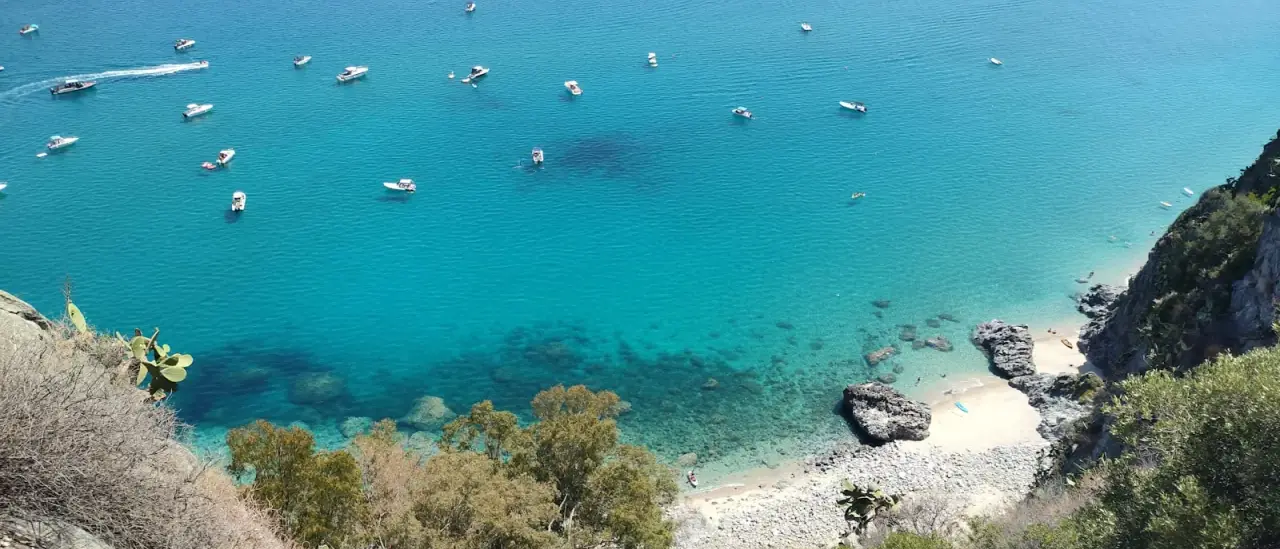 Piccole imbarcazioni ancorate in una cala turchese della costa calabrese