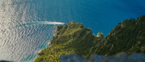 Una barca naviga sotto le coste verdi di Capri nel mare azzurro
