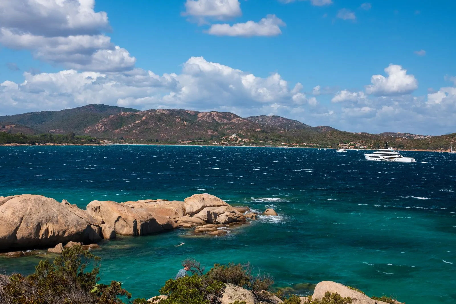 Costa rocciosa della Sardegna con acque turchesi e uno yacht all'ancora