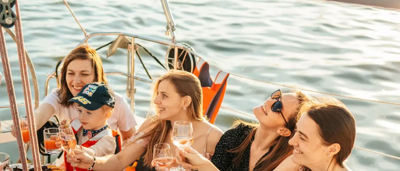 Gruppo di amici brinda a bordo di una barca a vela con tavola imbandita al tramonto