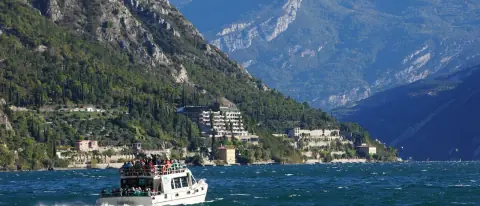 Barca di linea con passeggeri a bordo naviga sul Lago di Garda vicino a Limone, montagne sullo sfondo