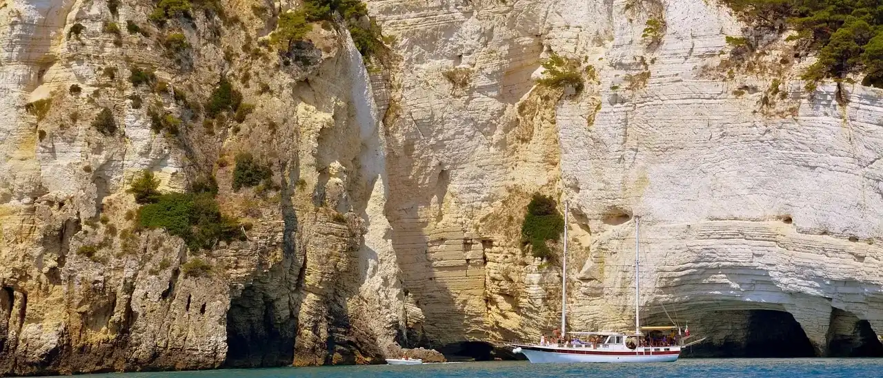 Barca da escursione sotto le falesie calcaree della costa del Gargano
