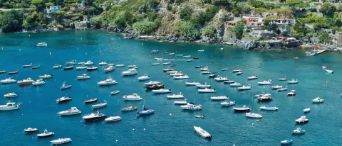 Decine di piccole barche ormeggiate in una baia turchese di Ischia vista dall'alto