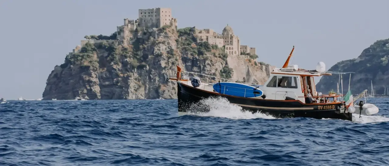 Piccola barca in navigazione davanti al Castello Aragonese di Ischia durante un giro dell'isola