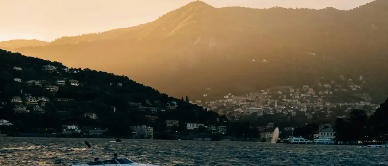 Piccola barca a motore al tramonto sul Lago di Como con un borgo lacustre sullo sfondo