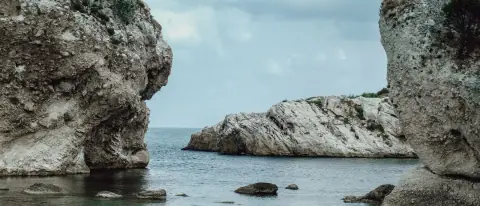 Costa rocciosa mediterranea con acqua limpida, insenatura riparata tra pareti di roccia chiara e persone in acqua