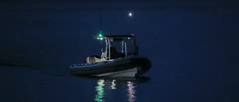 Piccolo gommone in navigazione notturna con luce laterale verde visibile e riflesso sull'acqua scura