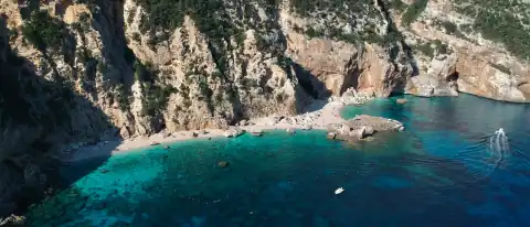 Una barca all'ancora nelle acque turchesi di una cala ai piedi di alte falesie