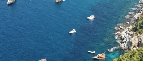 Barche a motore e a vela all'ancora nelle acque blu di una baia lungo una costa rocciosa
