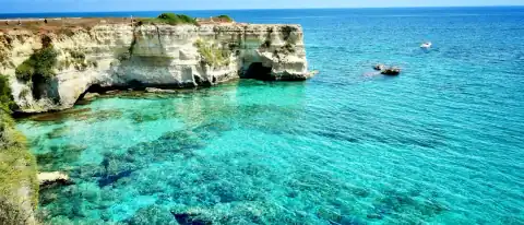 Una piccola barca tra gli scogli e l'acqua turchese della costa di Otranto, ai Faraglioni di Torre Sant'Andrea