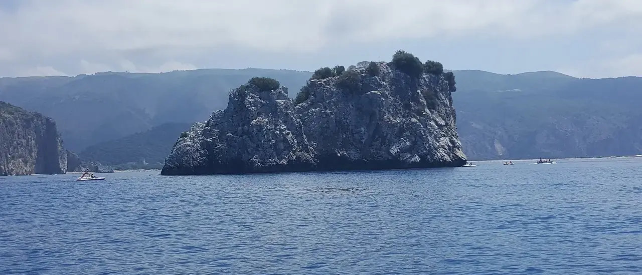 Lo scoglio roccioso di Capo Palinuro nel mare blu del Cilento, con piccole barche al largo