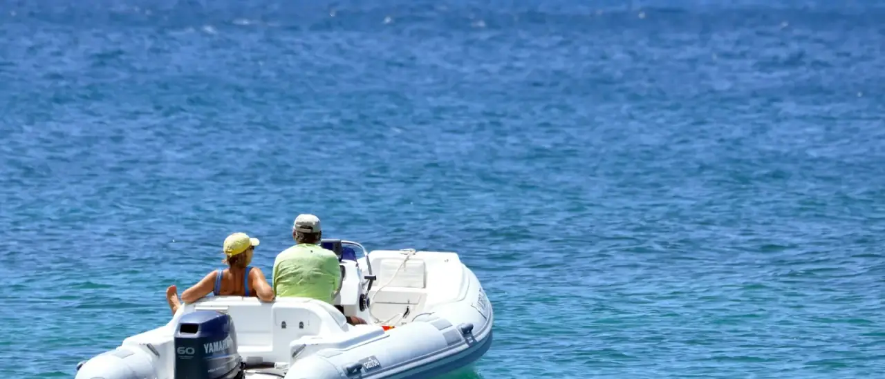 Coppia a bordo di un gommone in navigazione su mare azzurro lungo la costa
