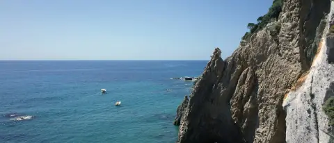 Piccole barche a motore in navigazione sottocosta lungo una falesia, con il mare aperto sullo sfondo
