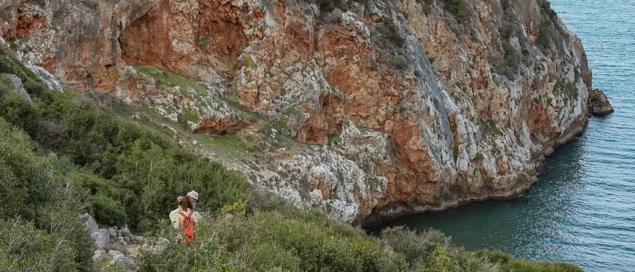 Sentiero escursionistico tra la macchia mediterranea con scogliera rocciosa e mare cristallino