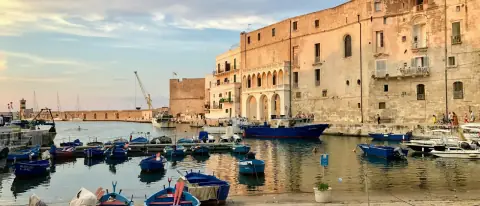 Porticciolo pugliese con edifici in pietra chiara e piccole barche da pesca colorate