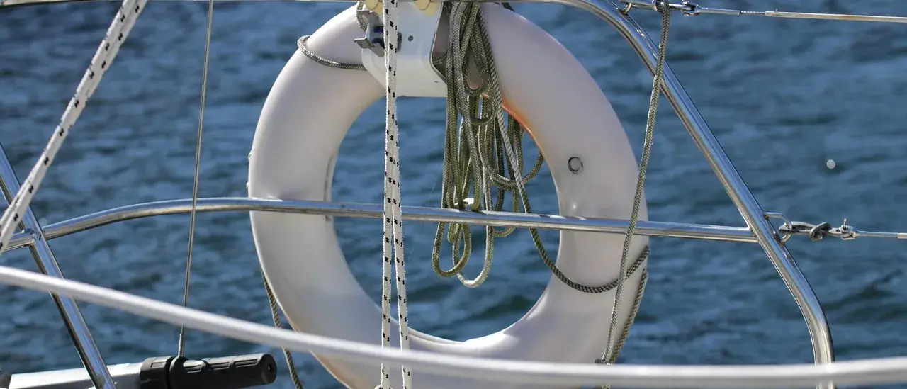 Salvagente anulare bianco con cima stivata, fissato al pulpito di una barca a vela sopra il mare aperto