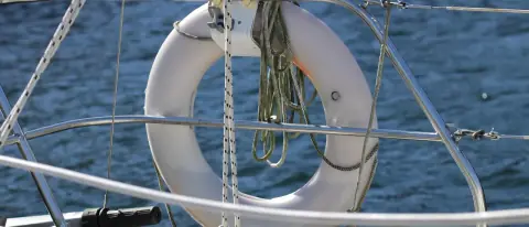 Salvagente anulare bianco con cima stivata, fissato al pulpito di una barca a vela sopra il mare aperto