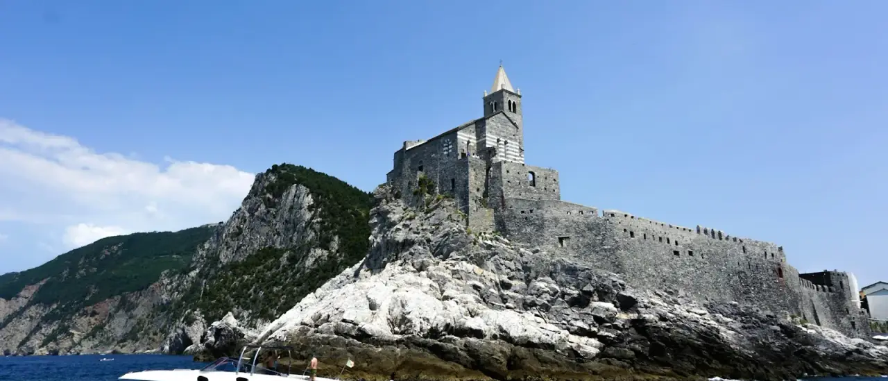 La chiesa di San Pietro a Portovenere sul promontorio roccioso, con una barca a motore che passa in primo piano