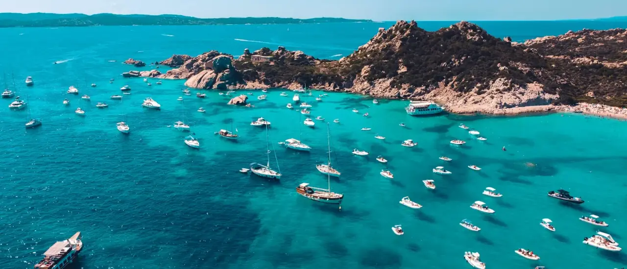 Numerose barche a vela e a motore all'ancora nelle acque turchesi di una cala della Sardegna