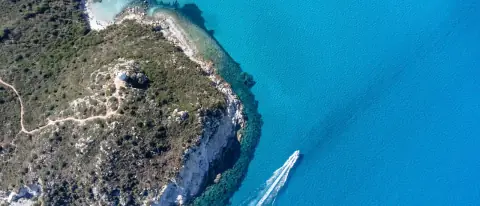 Una barca su acque turchesi lungo una costa rocciosa della Sardegna