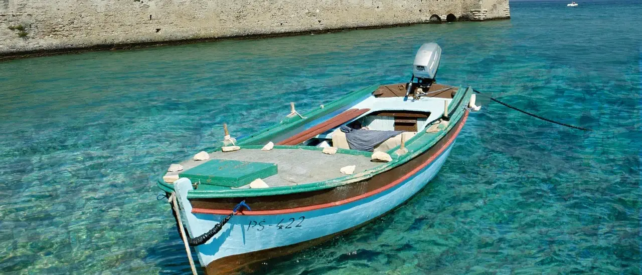 Barca in legno ormeggiata sull'acqua turchese davanti alle mura del castello Scaligero di Sirmione